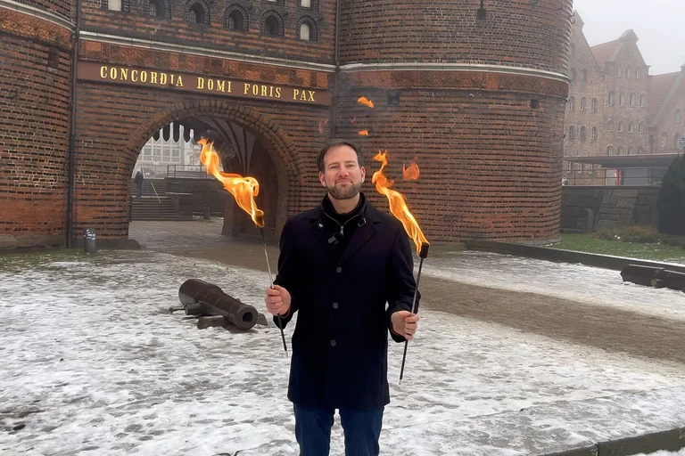 Ein Mann steht mit zwei brennenden Fackeln vor dem Lübecker Holstentor.