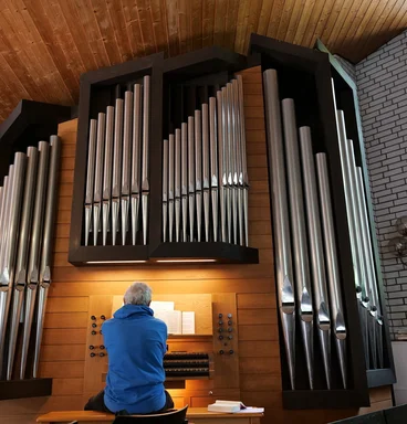Eine Orgel mit Orgelpfeifen in einem Gottesdienstraum, es sitzt eine Frau an der Orgel