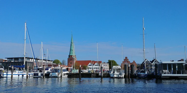 Eine Kirche am Wasser, davor Motorboote und Seegelboote