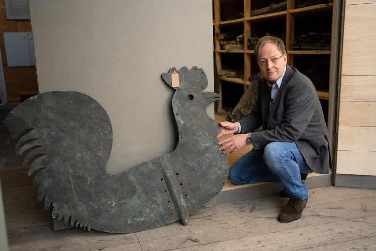 Ein Mann kniet neben einem Wetterhahn