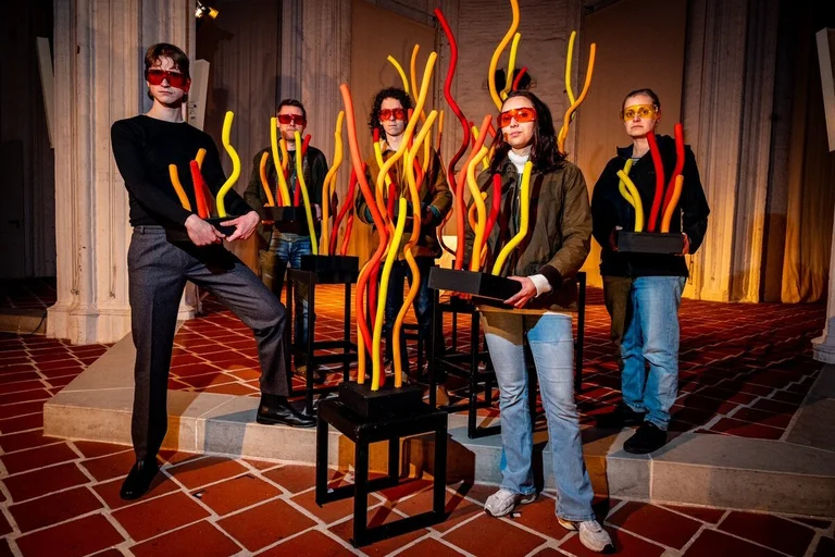 Eine Gruppe junger Menschen trägt bunte Brillen und hält flammenartige Skulpturen in den Händen.