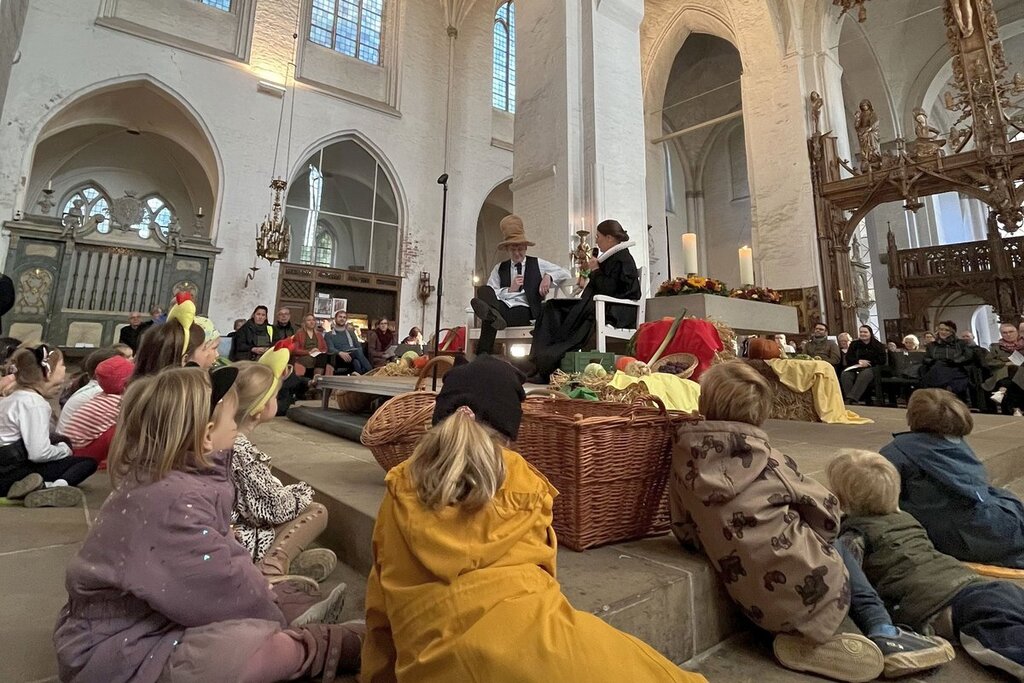Kinder liegen und sitzen rund um einen Altar vor dem eine Pastorin und Pastor etwas erzählen..