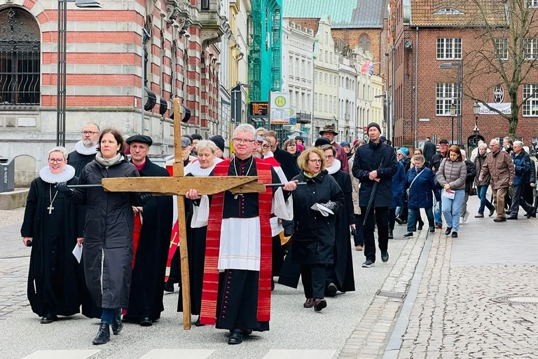 Menschen laufen in einer Prozession hinter einem Holzkreuz durch die Altstadt.
