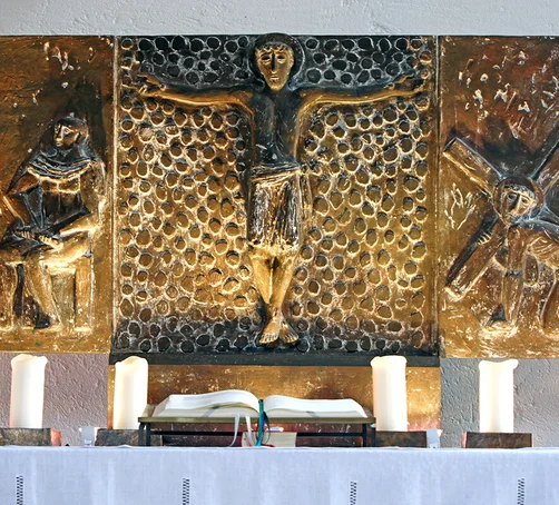 Bronze-Relief der Passion auf Altar, Künstler Fritz Fleer, unten 4 Kerzen neben offener Bibel, gelbe Strahler ein