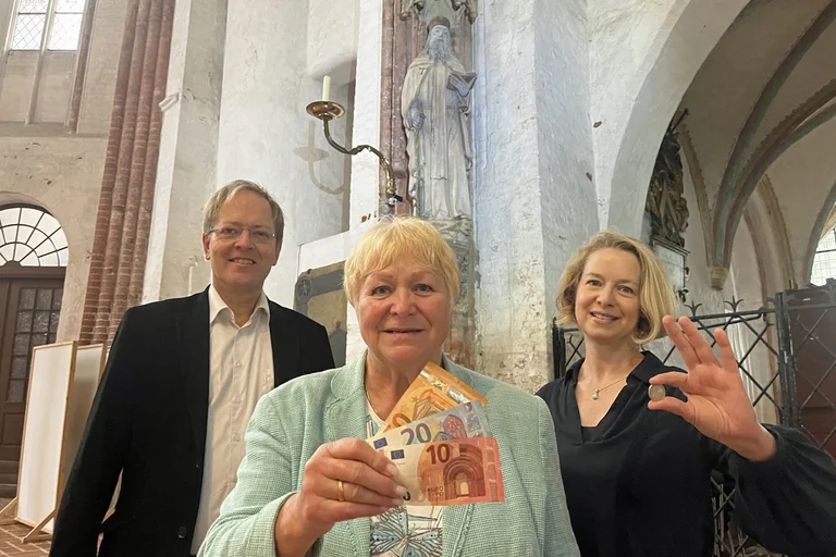 Zwei Frauen und ein Mann stehen in einer alten Kirche.