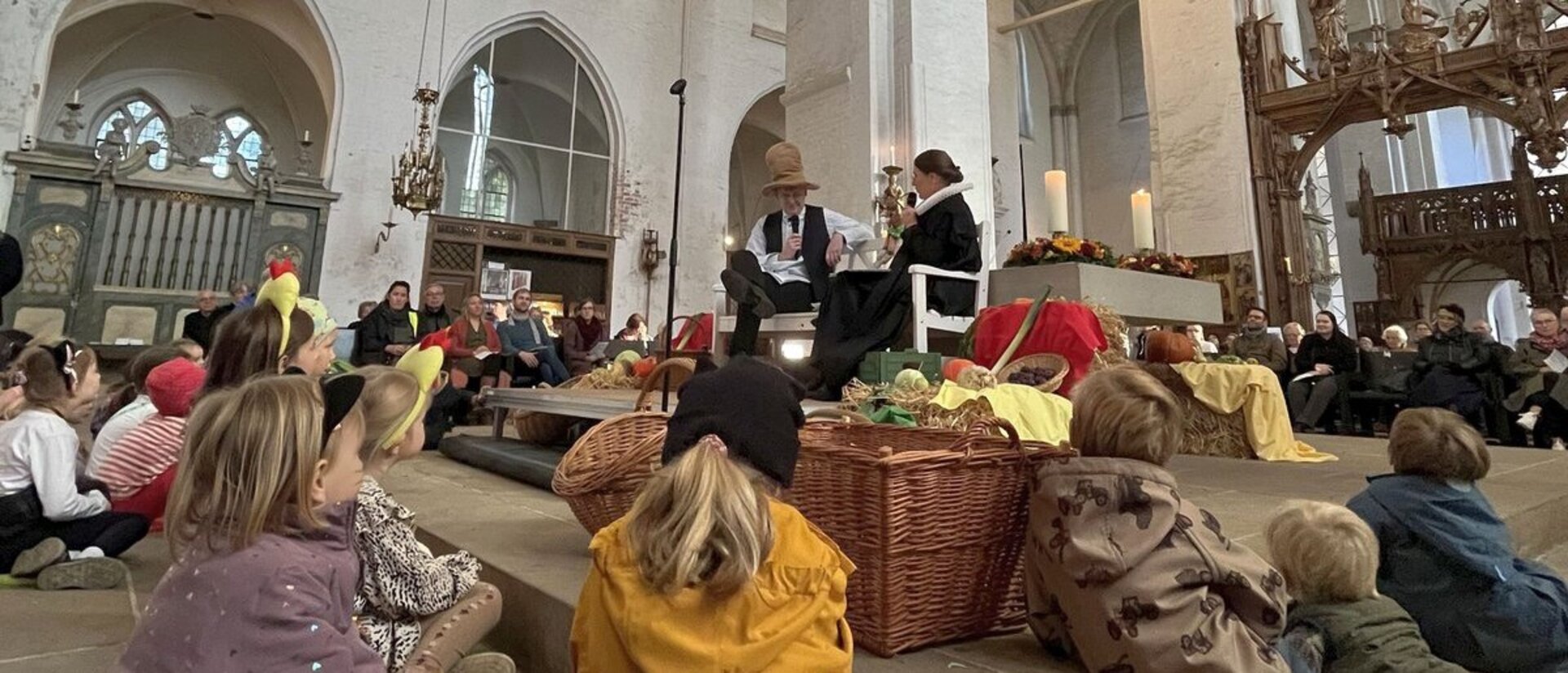 Kinder liegen und sitzen rund um einen Altar vor dem eine Pastorin und Pastor etwas erzählen..