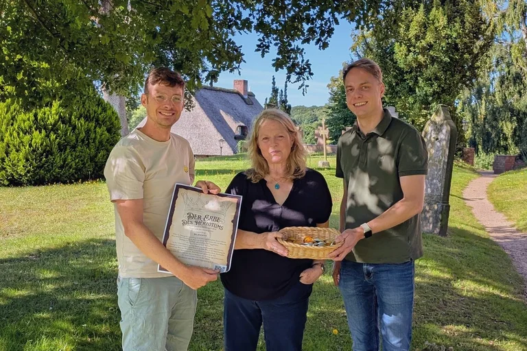 Drei Menschen stehen auf dem Berkenthiner Friedhof und schauen in die Kamera
