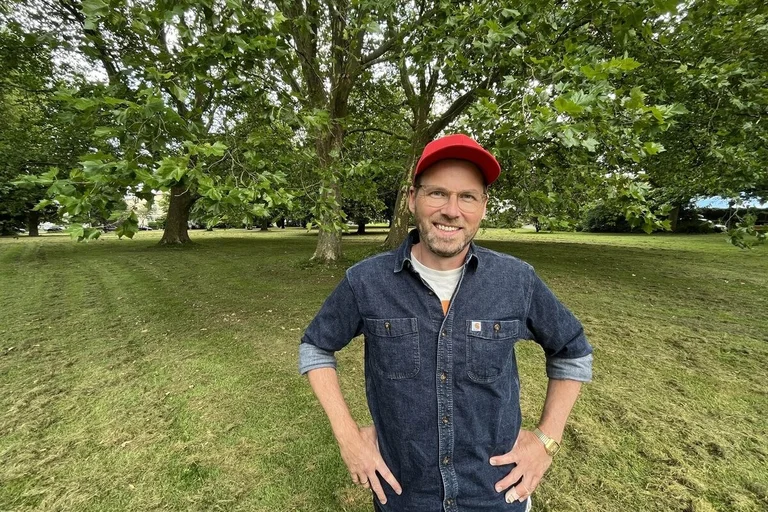 Junger Mann mit Basecap steht in einem grünen Park.