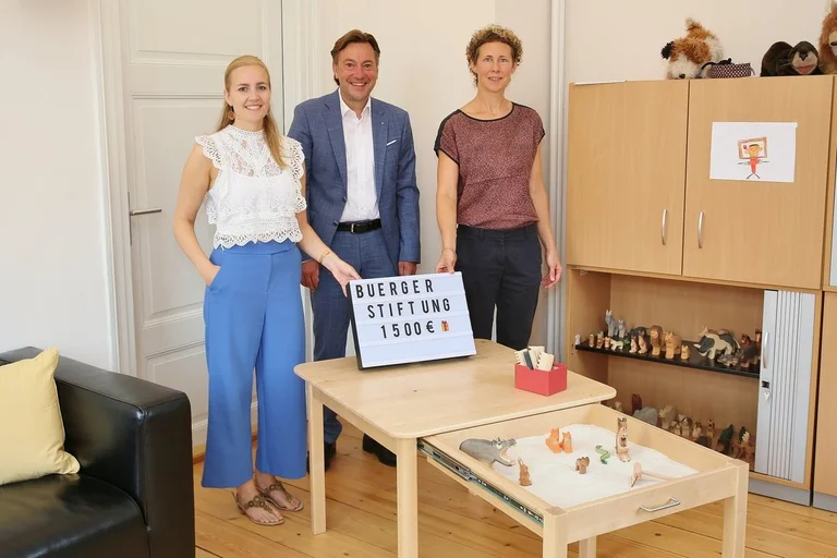 Menschen stehen lächelnd in einem Raum und zeigen ein Spielzeug. 