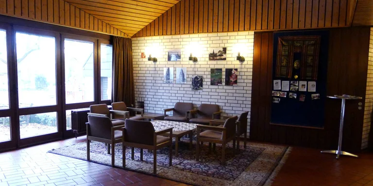 Die Sitzecke des Gemeindezentrums befindet sich im Flur direkt vor dem gGroßen Gemeindesaal. Sie hat durch eine Terassentür Zugang zum Garten. Gegenüber der Terassentür kommt man auch in die angrenzende Küche des Gemeindezentrums.   