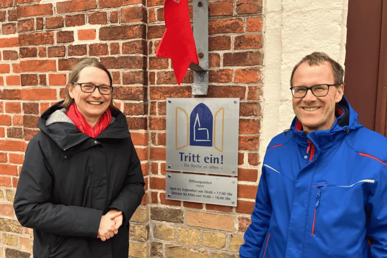 Zwei Menschen stehen lächelnd vor dem Eingang einer Kirche