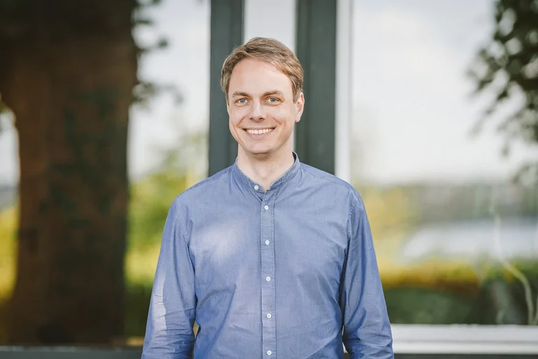 Ein Mann mit blauem Hemd lächelt in die Kamera.