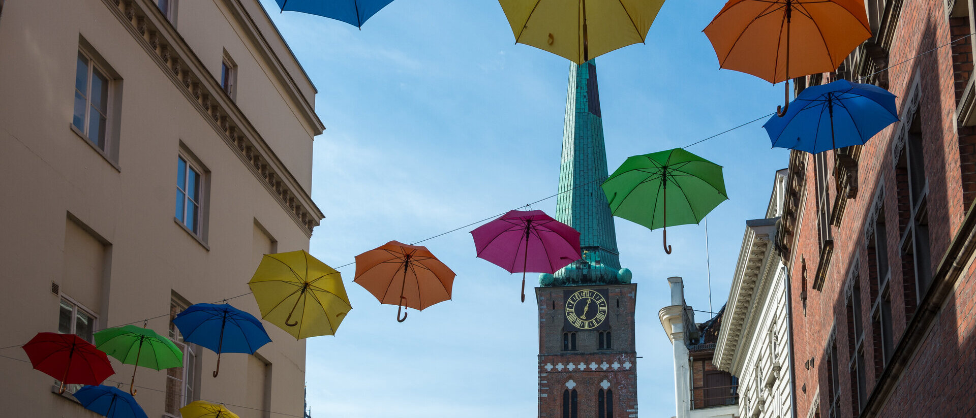 Aufgespannte Regenschirme in verschiedenen Farben, an mehreren Seilen aufgehängt - Im Hintergrund St. Jakobi Lübeck