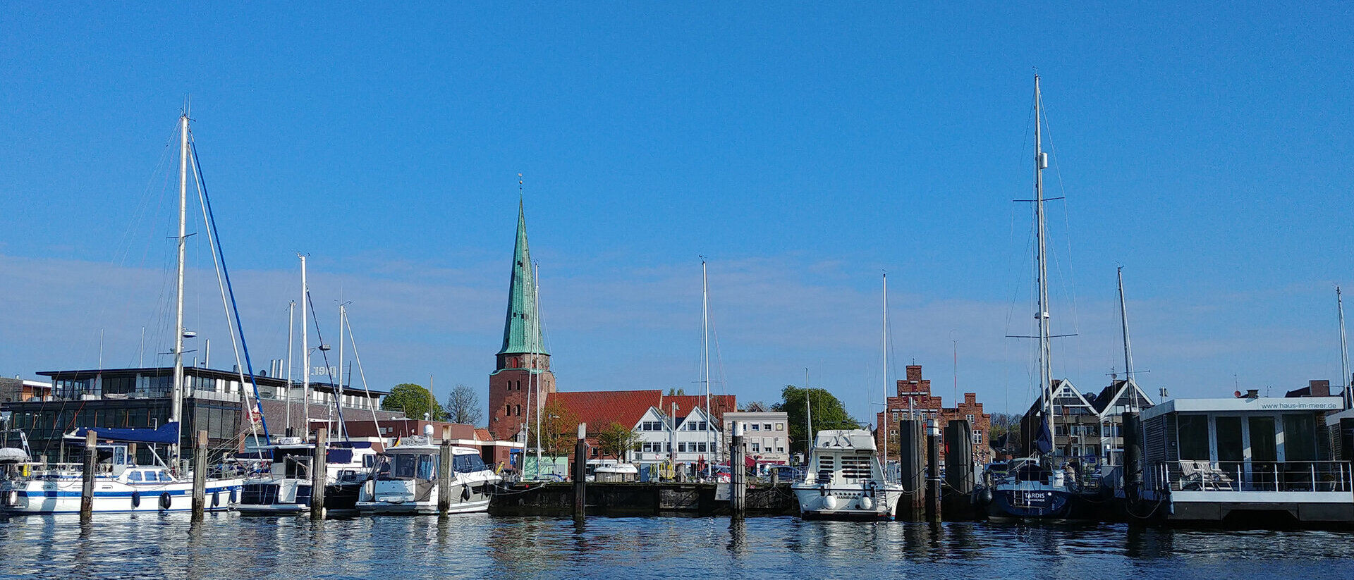 Eine Kirche am Wasser, davor Motorboote und Seegelboote