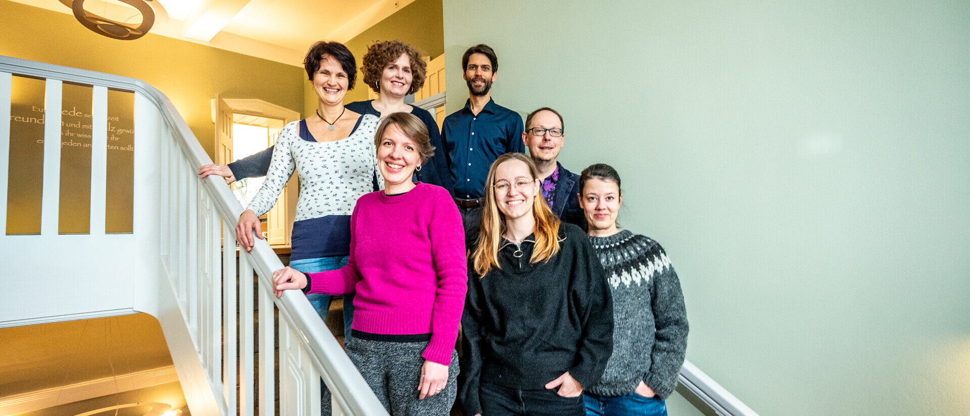 Eine Gruppe Menschen steht auf einer Treppe an einem weißen Treppengeländer.